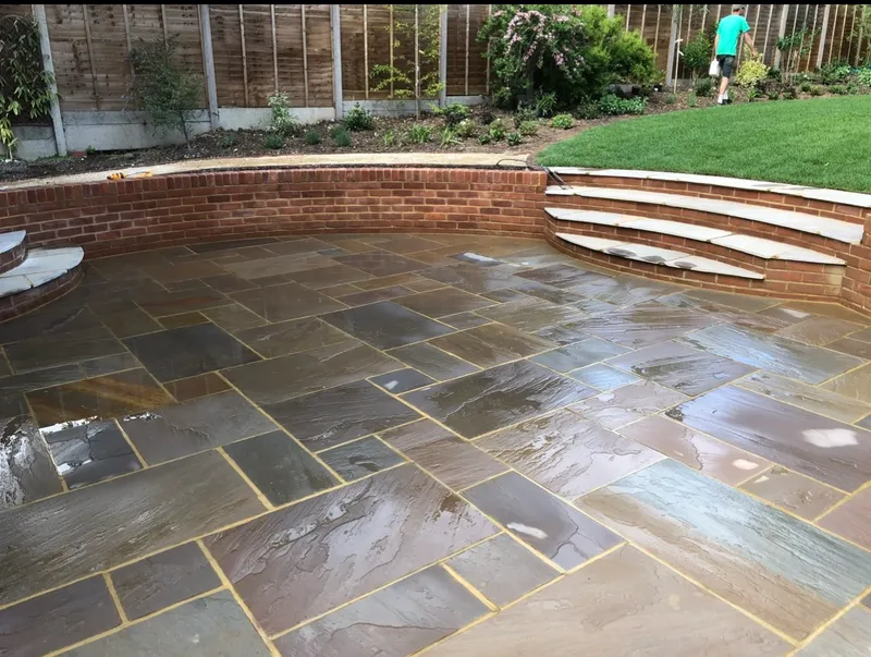 Curved red brick seating wall around a sandstone patio, with wide curved brick steps and stone treads up to the lawn