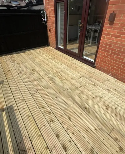 Pressure-treated timber decking laid against a red brick house, outside dark-framed patio doors