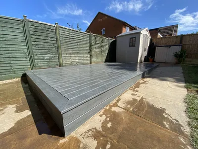Raised grey composite deck on a sandstone patio beside a garden shed