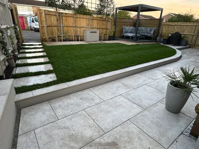 Large porcelain patio with a curved step down to the lawn and a pergola behind
