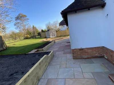 Sandstone patio along the back of the house, with raised beds, lawn and a summerhouse
