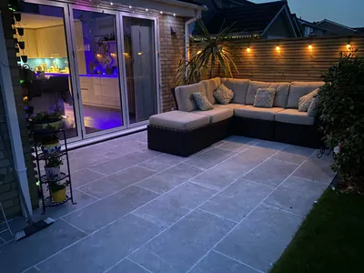 Grey stone patio with a corner sofa, lit up at dusk