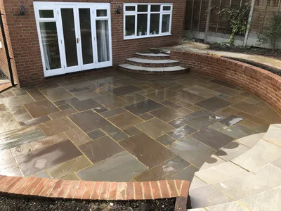 Sandstone patio by the house with a curved brick wall and steps