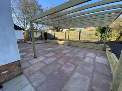 Timber pergola over a sandstone patio with a garden room behind