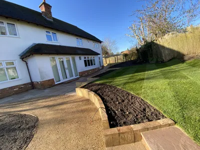 Curved timber sleeper raised bed between a gravel terrace and the lawn