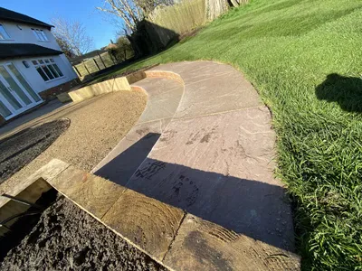 Curved sandstone steps leading from a gravel seating area up to the lawn