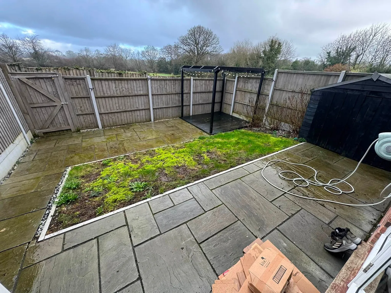 Hazlemere back garden before the makeover, with worn paving, a patchy lawn and old panel fencing