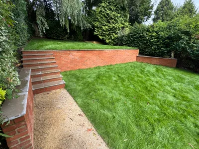 Curved red brick retaining wall with stone-capped steps up to a raised lawn