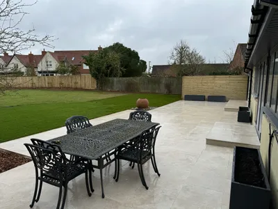 Large pale porcelain patio with an outdoor dining set beside a new lawn