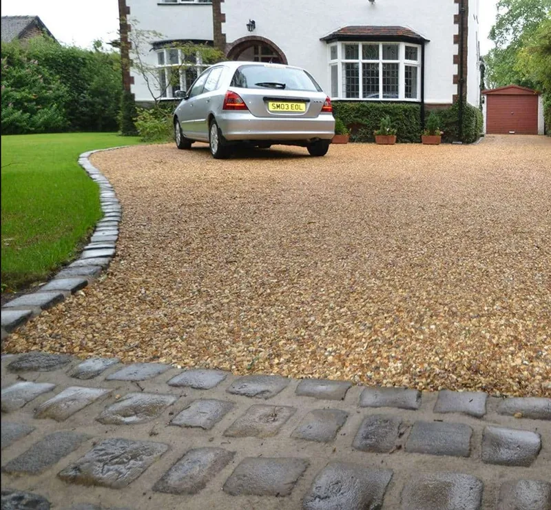 Golden gravel driveway edged with granite setts, curving past a lawn to a white rendered house