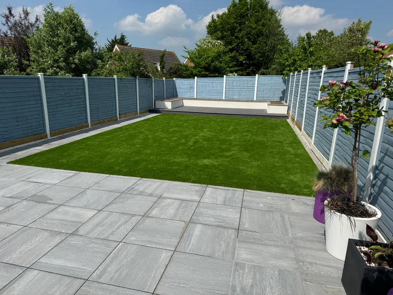 Fake grass lawn between a grey porcelain patio and grey painted fencing with white concrete posts