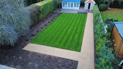 Newly laid striped lawn edged by a resin-bound path, with young hedging, a summer house and a deck at the end of the garden