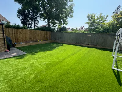 Bright green fake grass across a family garden with a football goal, timber fencing and a raised sleeper bed