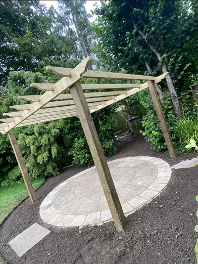 Circular paved patio feature beneath a timber pergola, surrounded by freshly dug borders