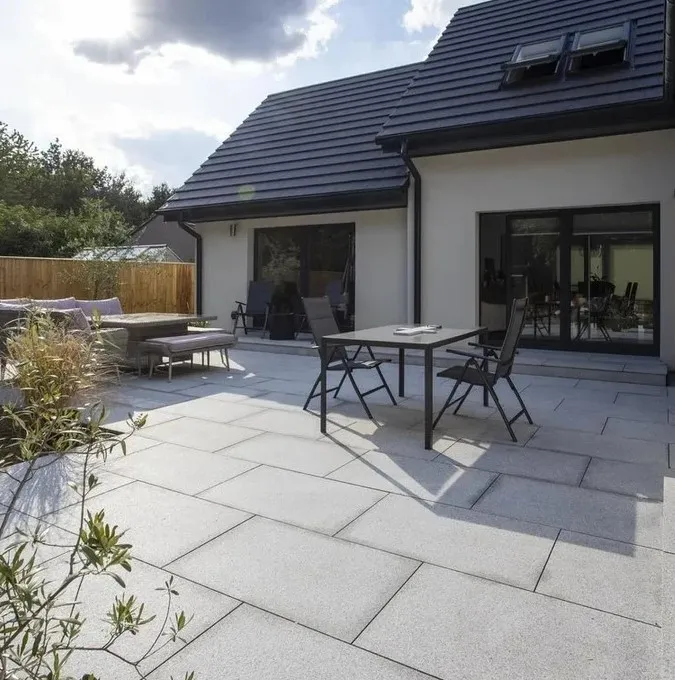 Pale grey granite patio with an outdoor dining table, behind a white rendered house