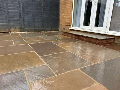 Warm-toned sandstone patio with a brick step up to French doors, beside a grey fence