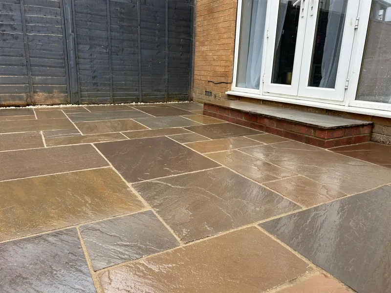 Warm-toned sandstone patio with a brick step up to French doors, beside a grey fence