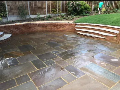 Curved brick retaining wall with wide stone steps up to a lawn, above a sandstone patio