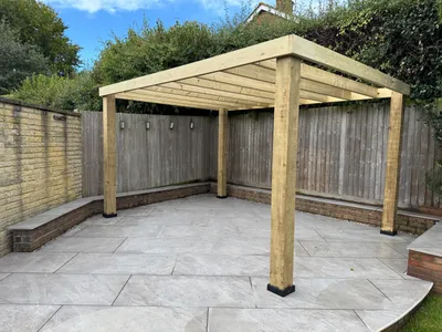 Pale grey paved patio with a curved edge, low brick seating walls and a timber pergola