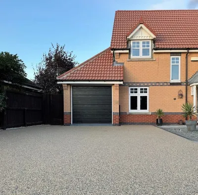Grey resin bonded driveway with a textured stone finish in front of a brick house and garage
