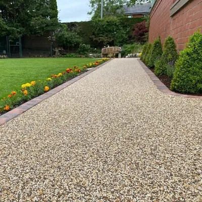 Resin bound path in a light stone mix with red brick edging, running between a lawn, bedding plants and clipped shrubs